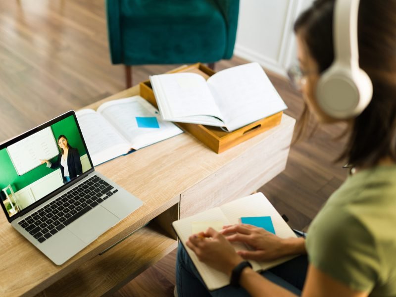 Rear view of a young college student paying attention and listening to her online teacher on the laptop at home